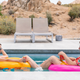 A woman and a man sit on colorful rafts in a swimming pool, facing each other with the desert in the background.